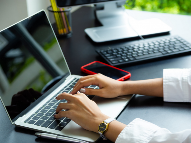 Hands at a laptop keyboard typing with modern accessories on the table